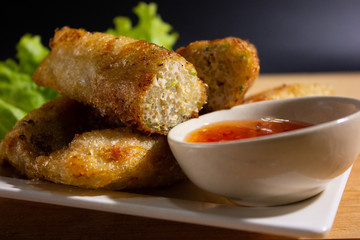 Fried spring rolls with chili sauce on wooden table.