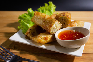 Fried spring rolls with chili sauce on wooden table.