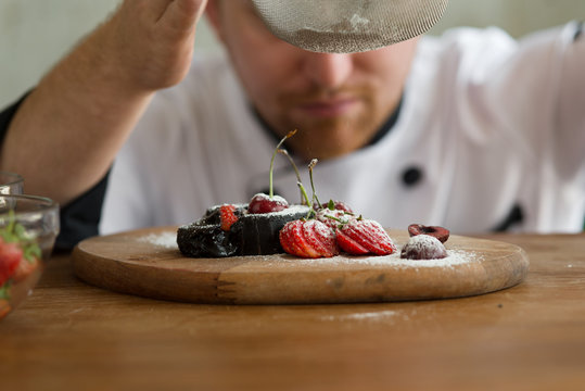 Pastry chef spreading icing sugar on chocolate cake.