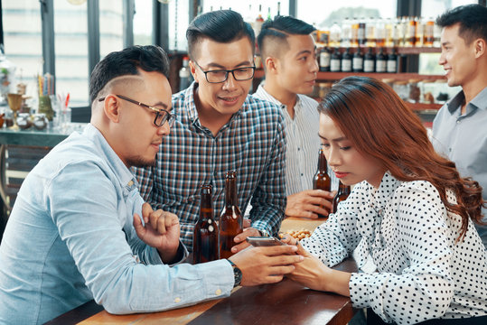 Colleagues discussing photo on smartphone when resting in pub after work