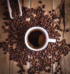 Close-up of black coffee in white cup, with coffee beans on wooden background, top view