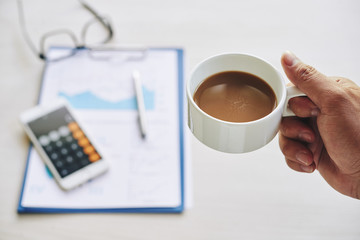 Hand of person drinking coffee before working with financial report