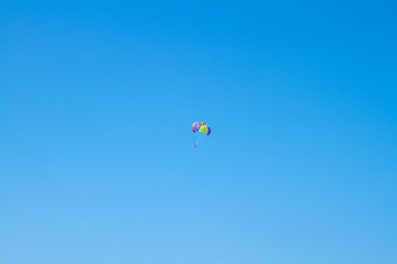A bright beach parachute in the blue sky in the distance. Fun on the beach. Flight over the sea on a parachute. The parachute hovers in the blue sky, tied to the boat.