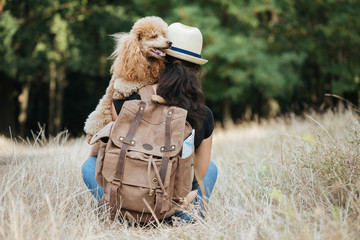 Woman traveler with backpack holding dog and looking at forest. Concept of travel. 