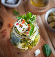 Close-up of marinated feta cheese in olive oil, herbs and red pepper flakes on wooden background 