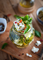 Close-up of marinated feta cheese in olive oil, herbs and red pepper flakes on wooden background 