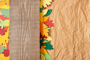 top view of wooden plank and colorful paper leaves arrangement on crumpled paper backdrop