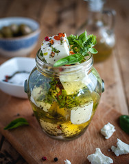 Close-up of marinated feta cheese in olive oil, herbs and red pepper flakes on wooden background 