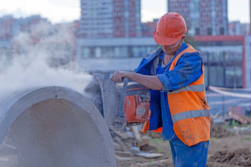 Worker at the construction site cuts the concrete ring for the well with a concrete cutter