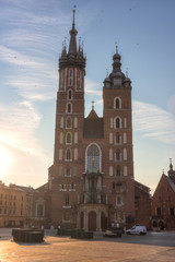 Fototapeta premium St. Mary's Basilica (Church of Our Lady Assumed into Heaven) on the Main Market square in Krakow at sunrise, vertical image with blue sky, sun and flying birds, Poland, Europe