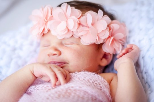 Cute sleeping newborn Caucasian baby girl a pink flower head bow. Sweet infant girl smiling in her sleep. A classical newborn infant photo session. First days of her life concept