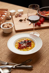 plate of delicious pasta with various ingredients and wine around on wooden table