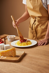 cropped shot of woman in apron putting pasta in plate on wooden table