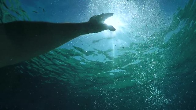 SLOW MOTION, HALF UNDERWATER, POV: Man lost at sea outstretching and trying to get to the surface while drowning on a sunny day. Male tourist suffocating and sinking to the bottom of the blue ocean.