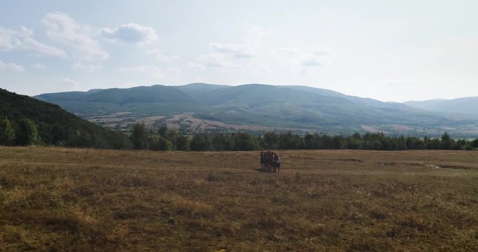 Aerial shot: Panoramic shot. A group of people in folk costumes goes up the hill