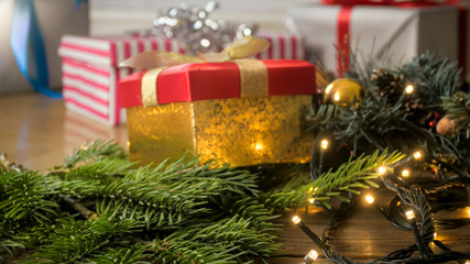 Closeup image of glowing light garlands and gifts in boxes lying on Christmas tree branches