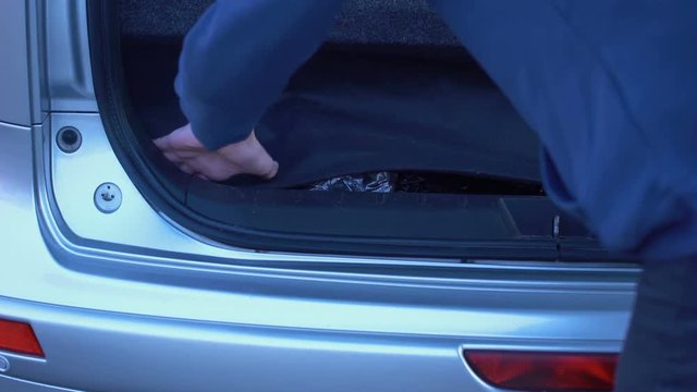 Man hiding forbidden packets in car trunk, drugs smuggling, illegal trading