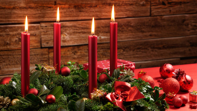 Advent wreath with four burning candles and festive decoration in front of a vintage wooden wall, studio shot with selective focus, copy space, no persons