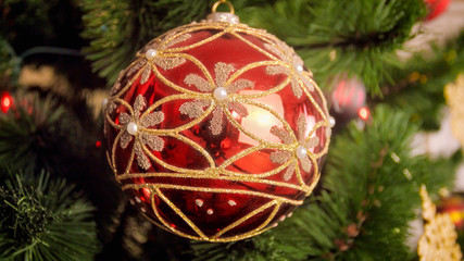 Closeup image of shiny red bauble with golden glitter on Christmas tree branch