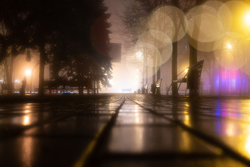 Alley of the evening misty park with burning lanterns, trees and benches. Night city autumn park