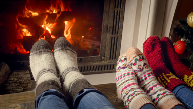 Closeup image of family with child wearing knitted woolen socks lying in living room with burning fireplace