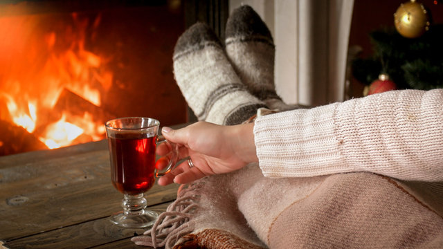 Closeup photo of young woman warming with hot tea at living room with burning fireplace