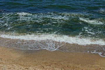 blue green sea waves with white foam on brown sand