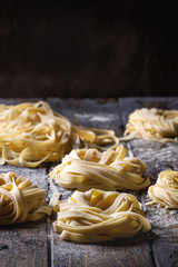 Variety of italian homemade raw uncooked pasta spaghetti and tagliatelle with semolina flour over dark plank texture wooden table. Dark rustic style