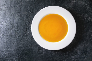 Plate of vegetarian vegan pumpkin carrot soup over black texture background. Flat lay, copy space