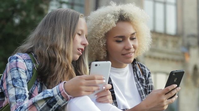 Undergraduate girls relaxing on lawn near school, bragging new modern smartphone