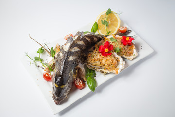 Backed dorada with salsa in shell, green, tomatoes, red flowers and lemon