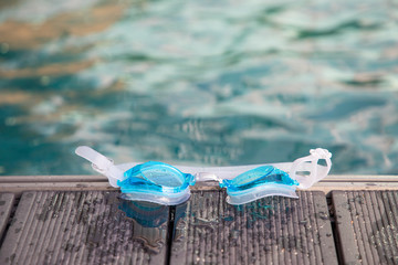 blue swimming goggles  on wooden floor  with sand  near swimming pool and sea background