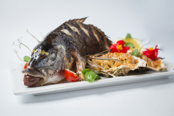 Backed dorada with salsa in shell, green, tomatoes, red flowers and lemon