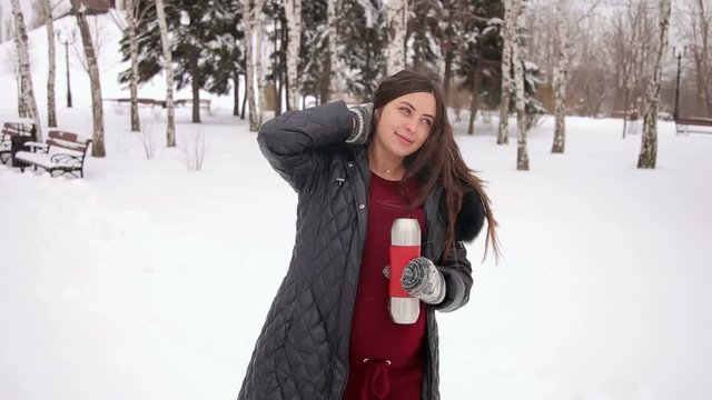 Pregnant girl with a thermos of hot tea in the winter Park. A young pregnant girl drinking tea in the winter in a snow-covered Park. Portrait of expectant mother. Pregnant woman in winter park.