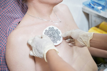 Tattoo artist putting stencil with beautiful drawing on chest of client