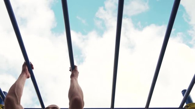 Slow Motion - Young Fit Man is Engaged in Street Workout. Male Athletic Man Doing Pull Ups on Parallel Bars. Summer Training in Park