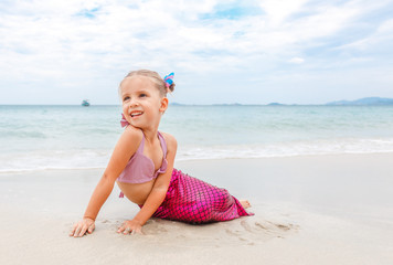 Little beautiful girl dressed in swimsuit as a mermaid sits on the seashore