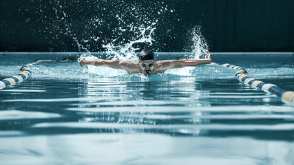 The dynamic and fit swimmer in cap breathing performing the butterfly stroke at pool. The young man. The fitsport, swimmer, pool, healthy, lifestyle, competition, training, athlete, energy concept