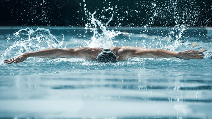 The dynamic and fit swimmer in cap breathing performing the butterfly stroke at pool. The young man. The fitsport, swimmer, pool, healthy, lifestyle, competition, training, athlete, energy concept - obrazy, fototapety, plakaty