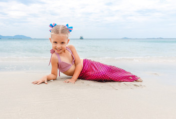 Little beautiful girl dressed in swimsuit as a mermaid sits on the seashore