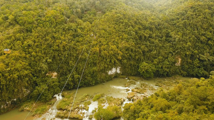 People have fun a zip line through a canyon with a river in the rainforest jungle. Aerial view, tourist attraction at the zipline attraction in the jungle on the island of Bohol. Travel concept.