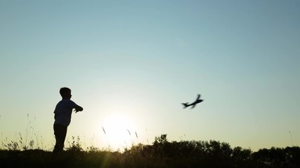 Video of black silhouette of young kid playing toy plane outside in countryside scenic landscape isolated at soft sunset sun light and blue sky background. Real time full hd footage.