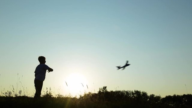 Video of black silhouette of young kid playing toy plane outside in countryside scenic landscape isolated at soft sunset sun light and blue sky background. Real time full hd footage.