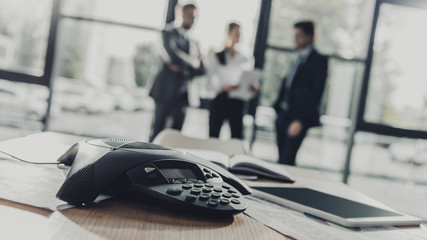close-up shot of conference phone with blurred business people on background at modern office
