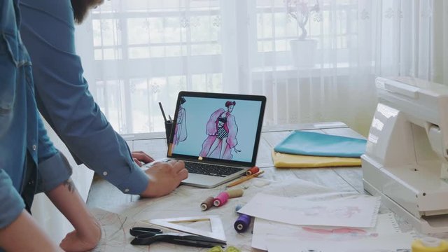 Small team of fashion designers choosing sketches on laptop computer