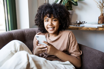 Young cute african-american woman using phone, sitting at a cafe holding a smartphone, answering...