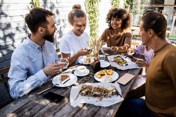 Group of young people sitting on a picnic blanket, having fun while talking interesting stories, international multietnicaly friendship concept.