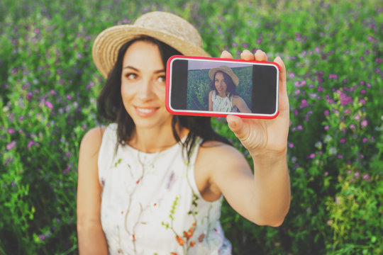 Beautiful young woman taking a selfie on the field of clover