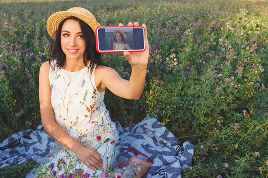 Beautiful young woman taking a selfie on the field of clover