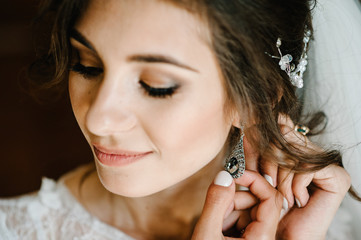 Obraz premium Wedding earrings on a female hand wear, she takes the earrings, the bride fees, morning bride, woman in white dress.